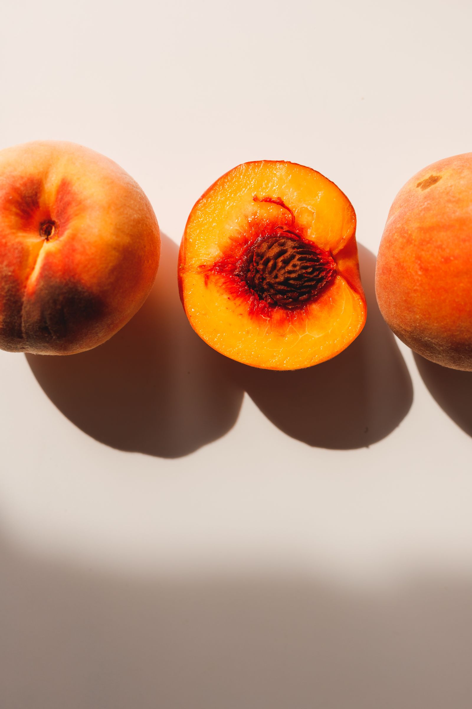 A ripe peach cut in half, resting in soft shadow on a plain surface