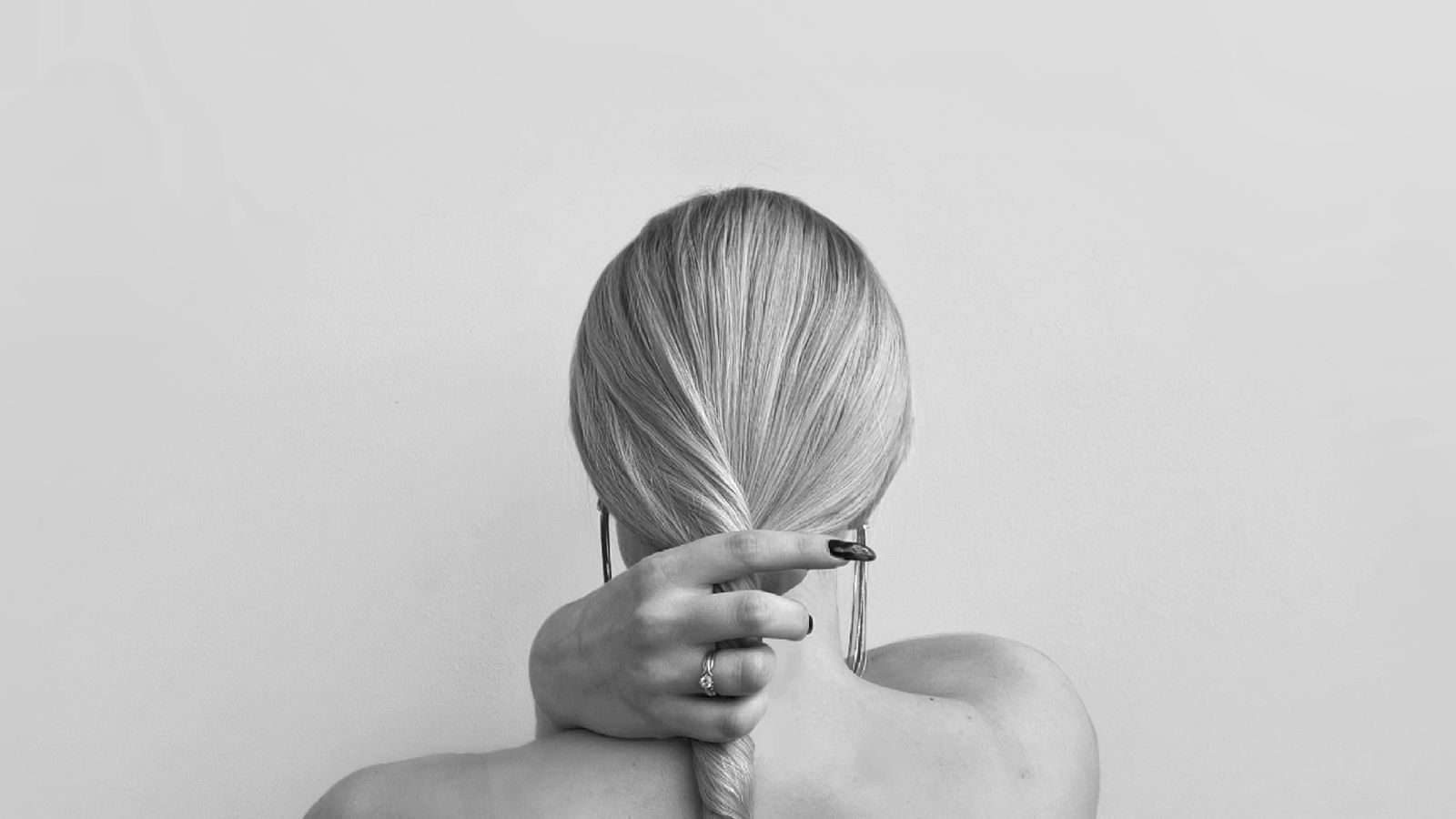 A woman seen from behind, hair gathered in a ponytail, against a quiet dark background