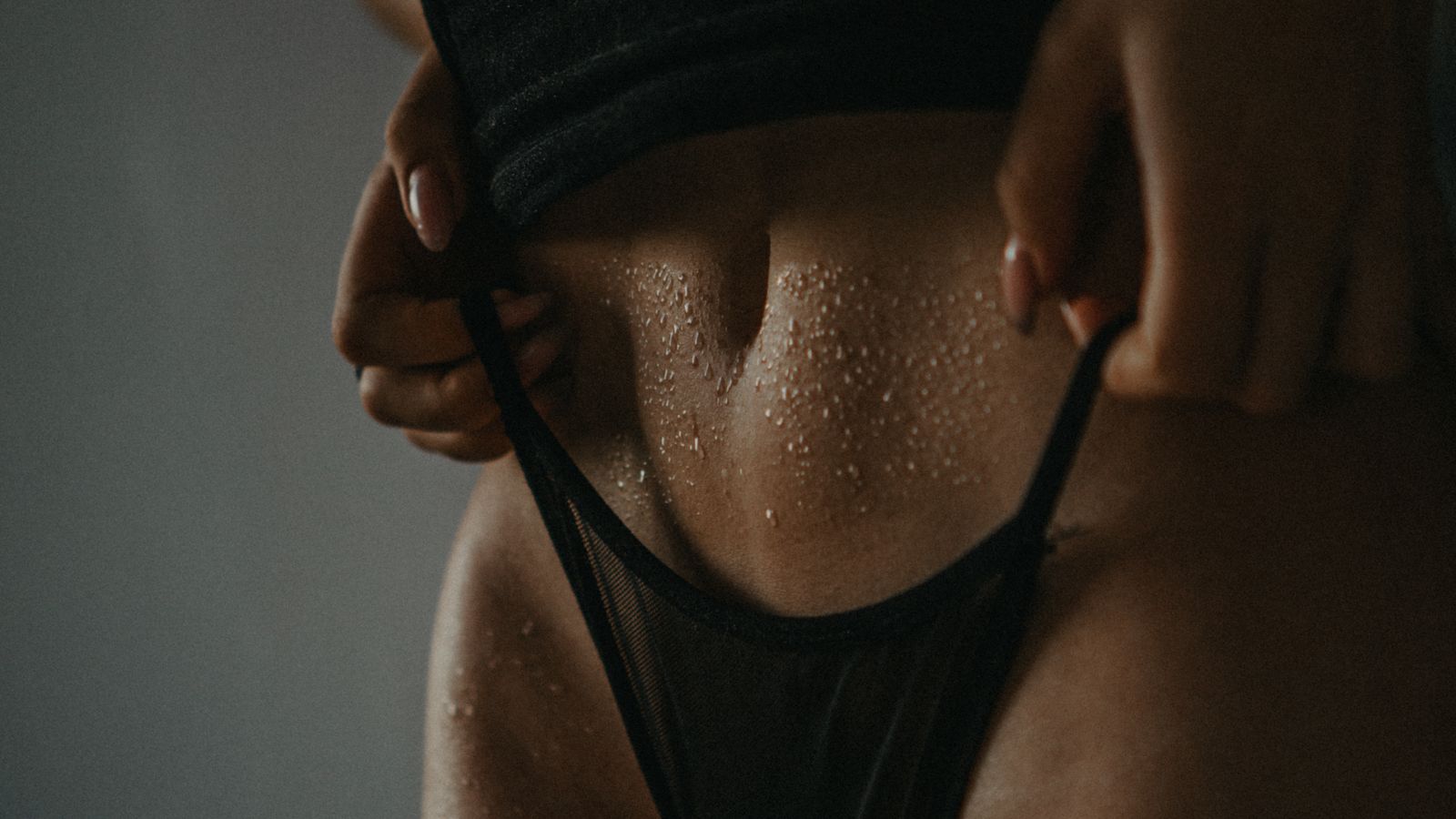 Skin beaded with sweat in low light as a hand slips a black strap loose.