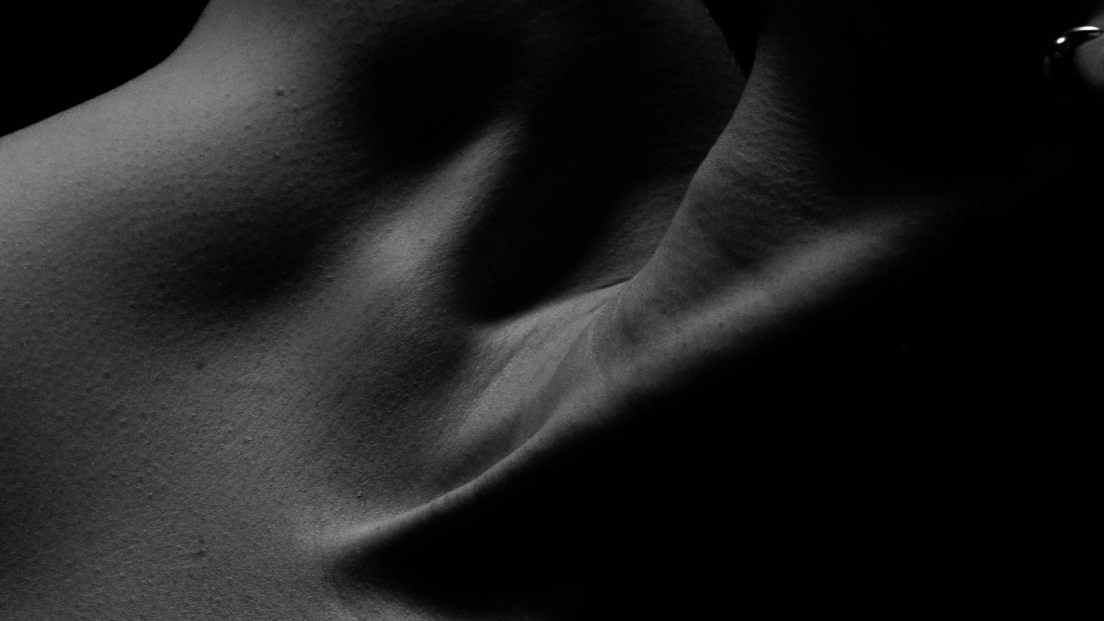 A figure in soft shadow, half lit, no face visible, in a warm dark room.
